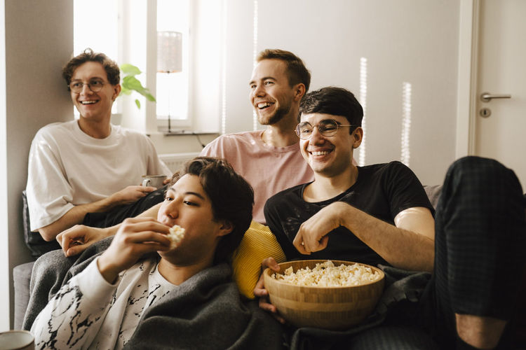 Smiling male friends eating popcorn while watching sports at home