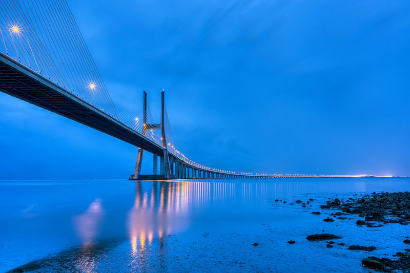 Bridge over sea against blue sky at dusk