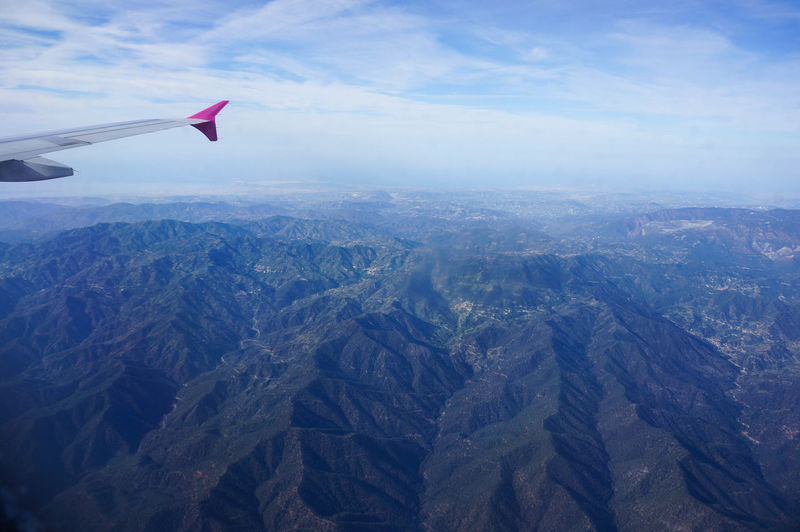 Cropped image of airplane flying over mountains against sky