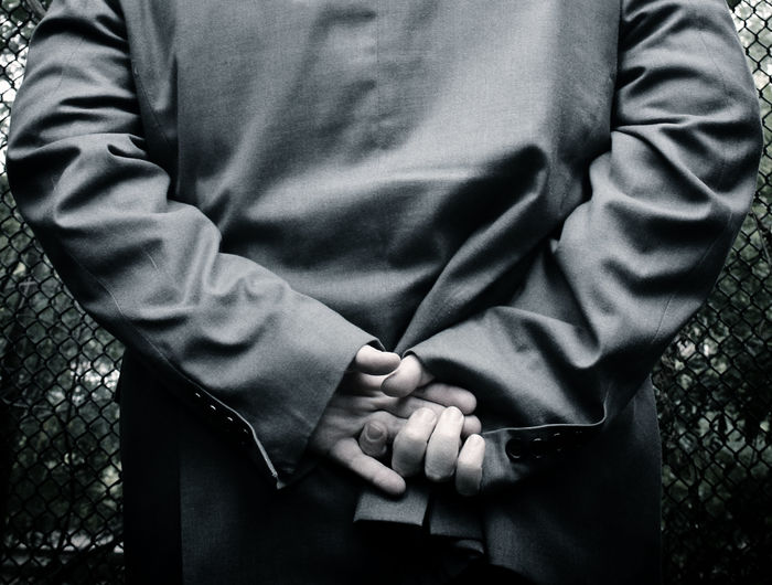 Midsection of man with hands behind back standing by fence
