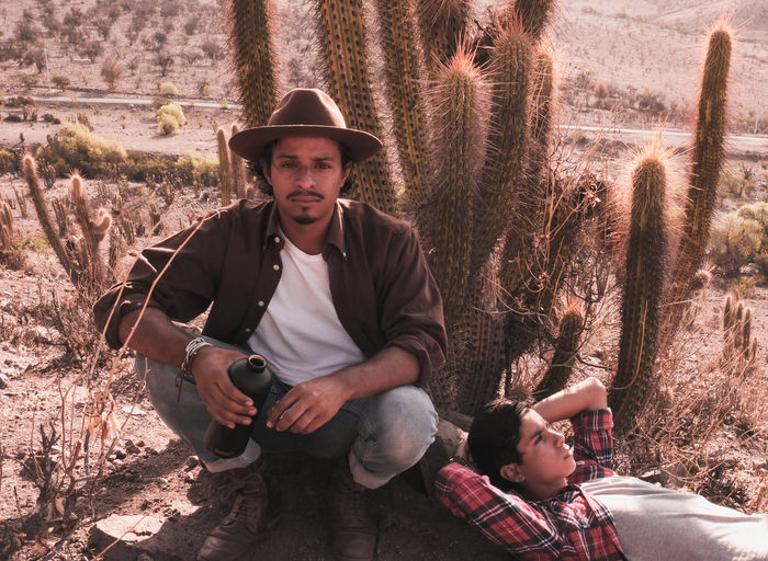 Portrait of young man sitting by cactus in desert