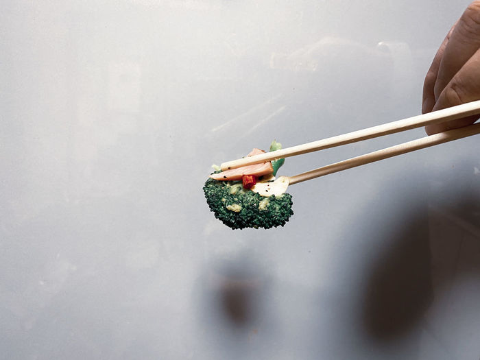 Close-up of person holding broccoli , chili pepper , garlic and bacon with chopsticks