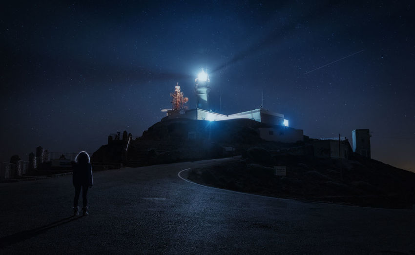 Rear view of woman looking at illuminated lighthouse at night