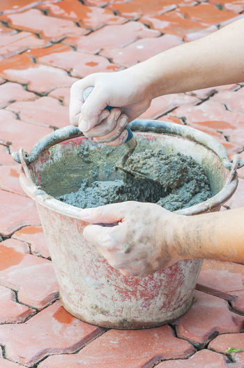 Cropped hands of man mixing cement in bucket on floor