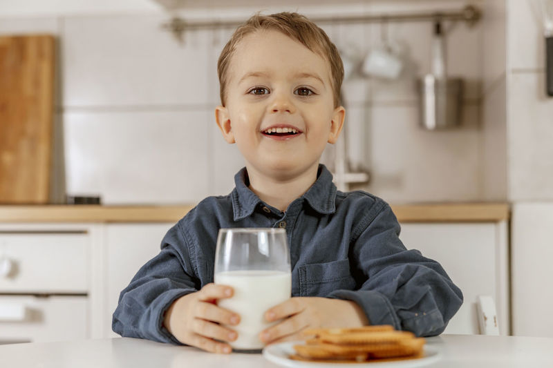 Little boy sitting in the kitchen and drinking milk. fresh milk in glass, dairy healthy drink. 