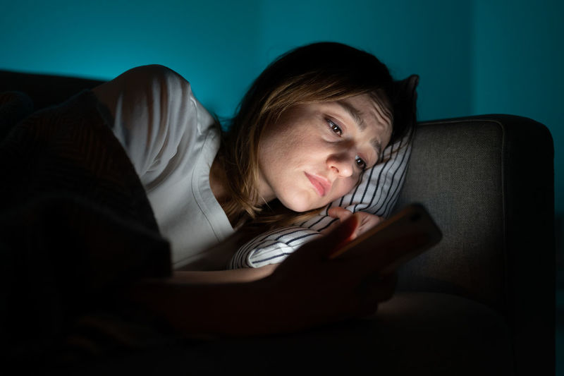 Woman using mobile phone while lying in bed at night, suffering from post-breakup insomnia. anxiety.