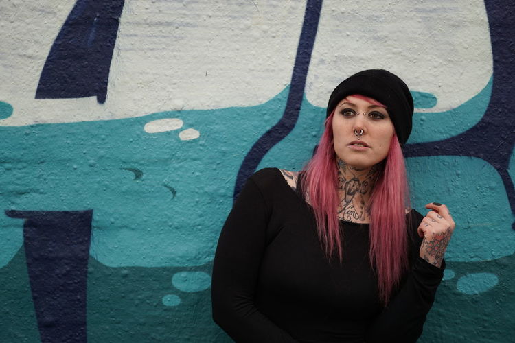Young woman with pink hair standing against graffiti wall