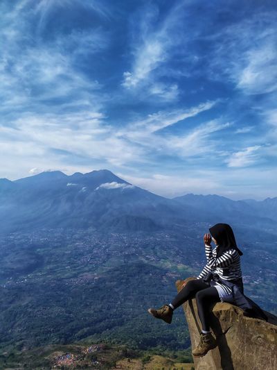 Woman sitting on mountain against sky