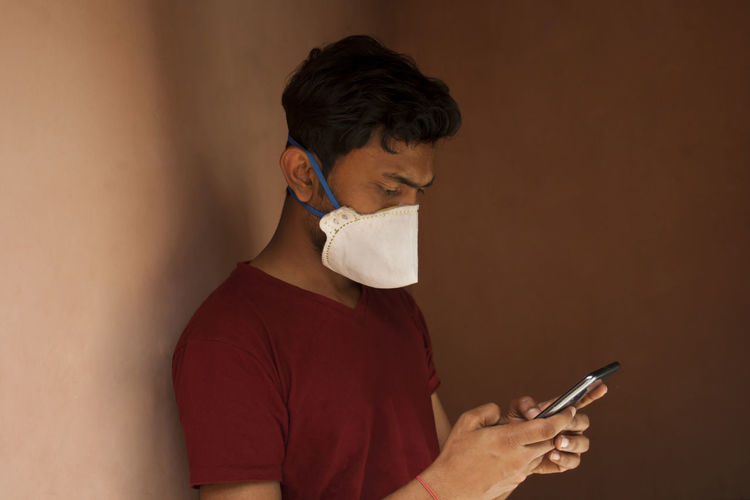 Young man wearing mask using mobile phone against wall