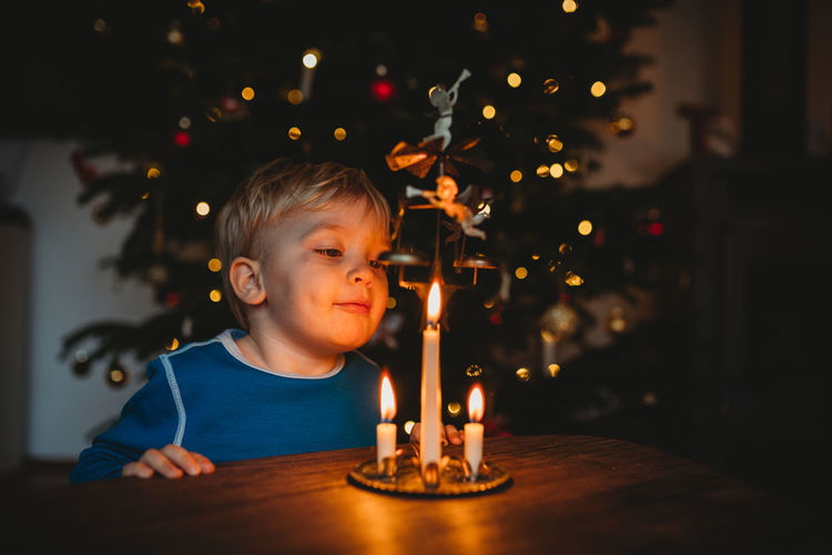 Little boy blowing candles from a christmas ornament with tree behind