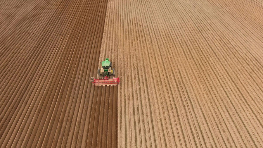 Aerial view of ploughed field with tractor sowing seeds of wheat.