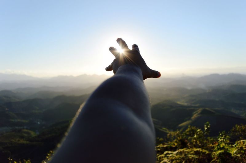 Cropped image of person hand reaching towards sun