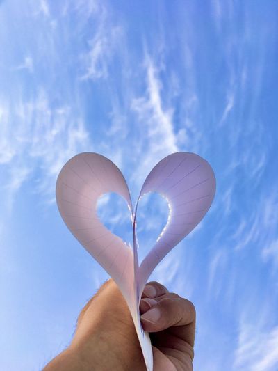 Person holding heart shape against sky