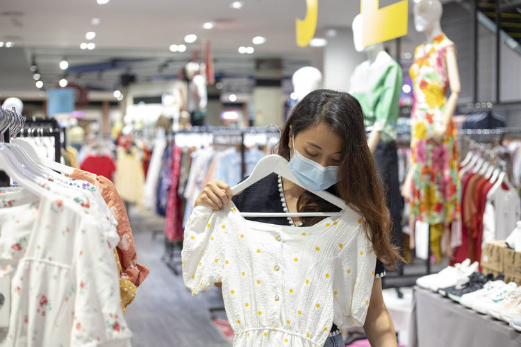 Young woman wearing mask shopping at clothing store