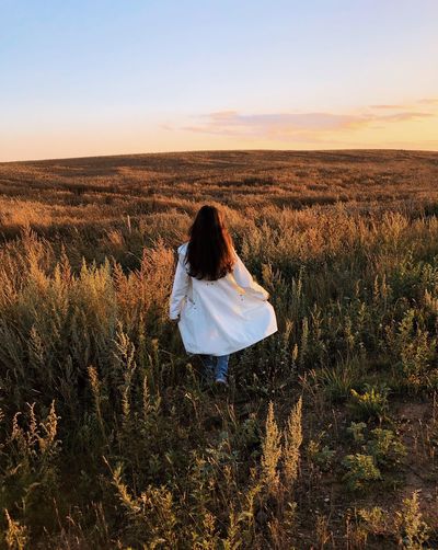 Woman in white coat walking in the field and watching sunset
