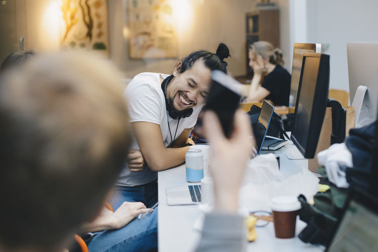 Happy computer programmer sitting with colleagues at desk in office