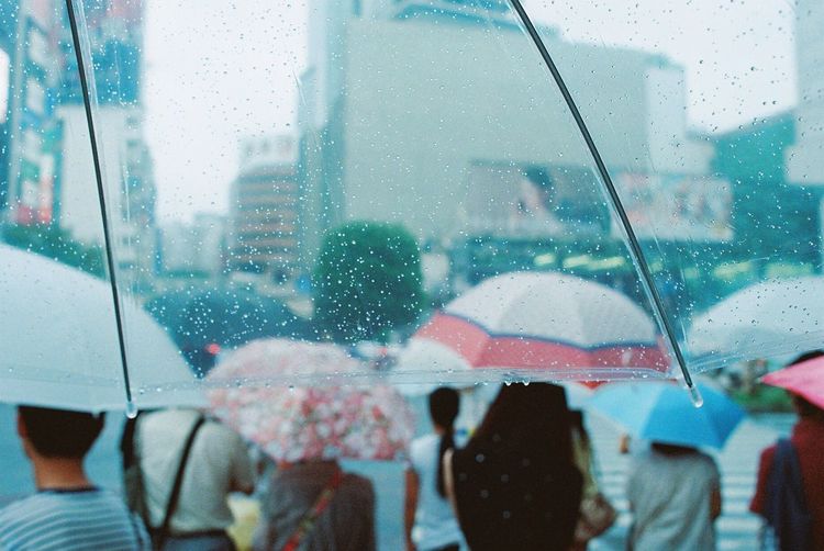 Cropped image of wet umbrella against people on road during rainy season
