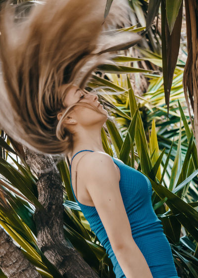 Side view of young woman tossing hair with palm leaves in plant