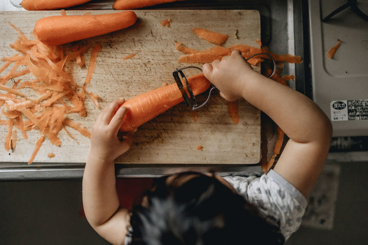 High angle view of a toddler peeling carrot 