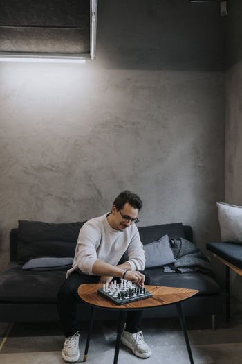 Young male entrepreneur playing chess while sitting on sofa at workplace