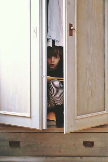 Portrait of cute boy hiding in closet at home
