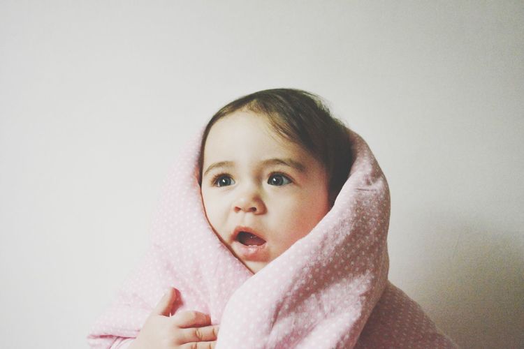 Cute baby girl warped in blanket against wall