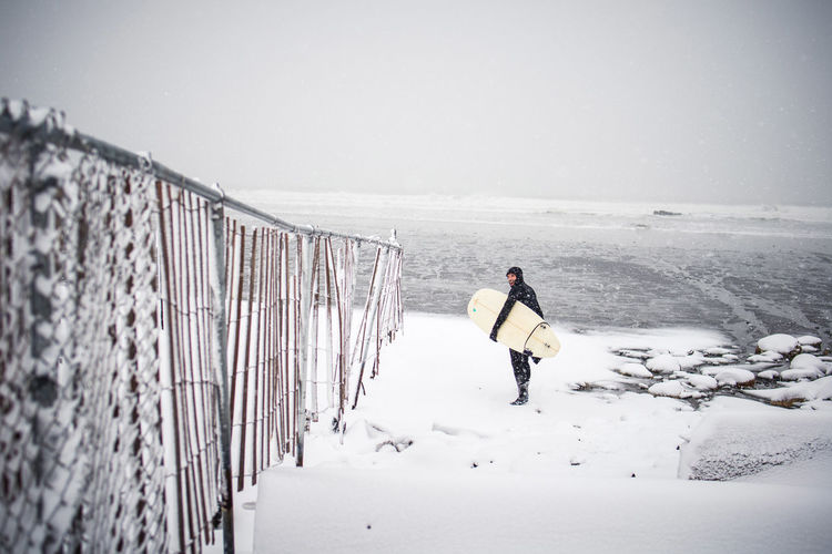 Surfer walking along the beach in maine during a winter snow storm