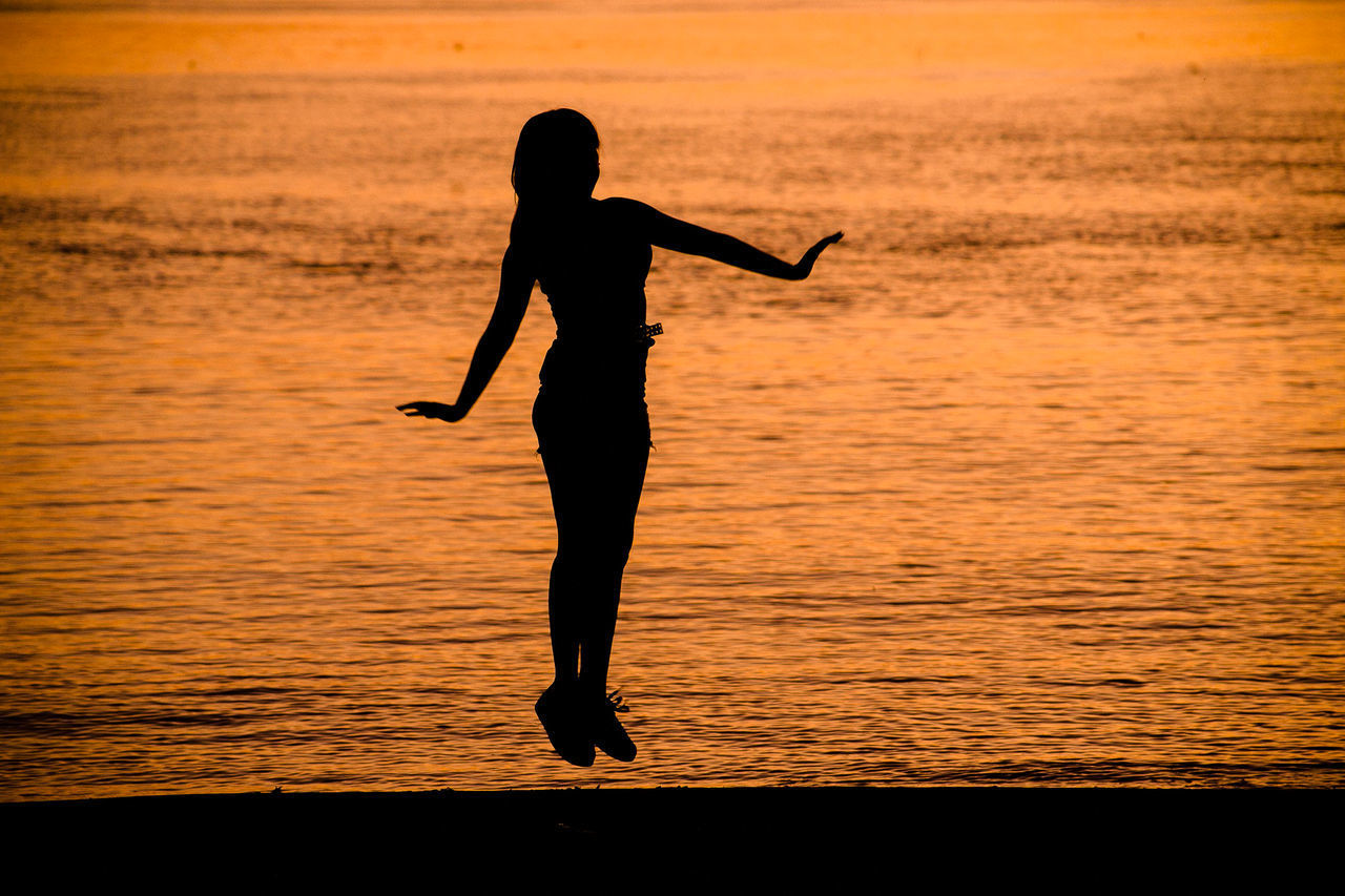 SILHOUETTE WOMAN STANDING BY SEA AGAINST ORANGE SKY