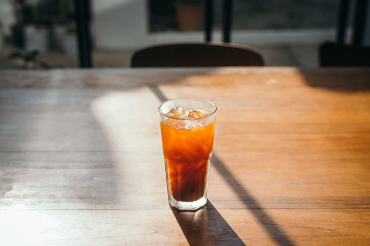 Iced americano coffee on wooden cafe table with sunlight