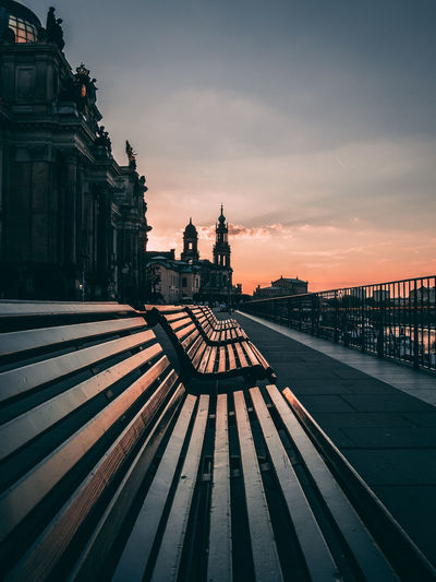 Empty benches in city against sky during sunset