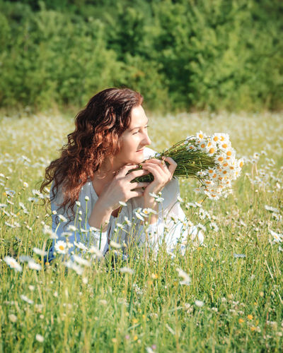 Side view of young woman sitting on grassy field