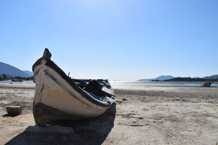 Abandoned boat on beach against clear blue sky
