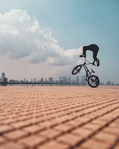 Man bmx cycling on promenade in city against blue sky