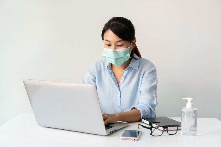 Woman wearing mask using laptop against gray background