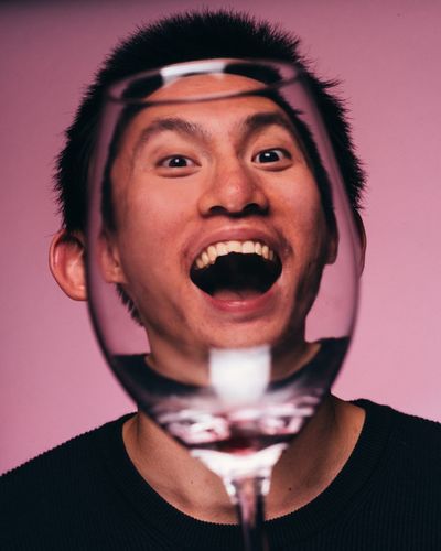 Close-up portrait of young man seen through wineglass against pink background