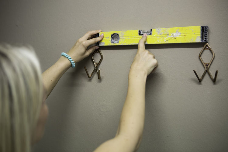Rear view of woman holding yellow spirit level on wall