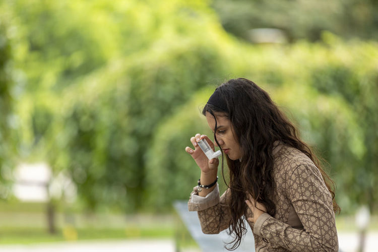 Teenager girl using asthma inhaler in park