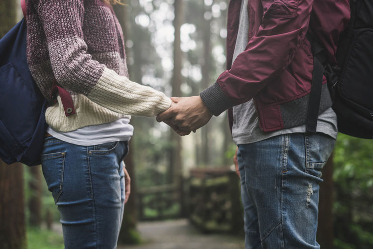Midsection of couple holding hands in forest