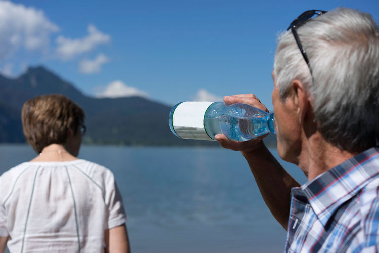 Senior man drinking water by woman near kocher lake against sky