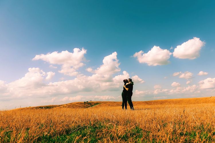 Couple kissing on grassy field against sky during sunny day