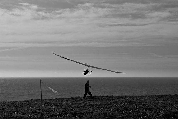Side view of man walking by hang glider flying above sea