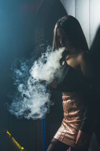 Portrait of woman smoking hookah while standing at home