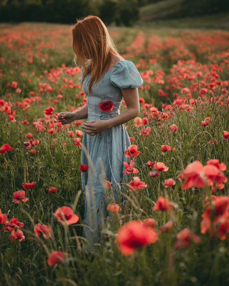 Rear view of young woman standing amidst flowers on field