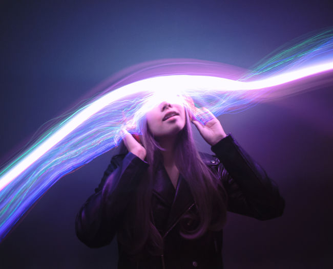 Digital composite image of light trails and young woman against colored background