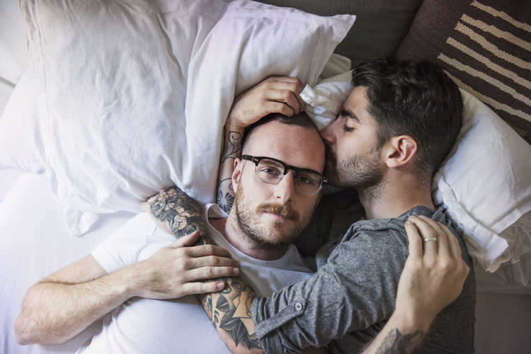 Man kissing boyfriend while lying on bed at home