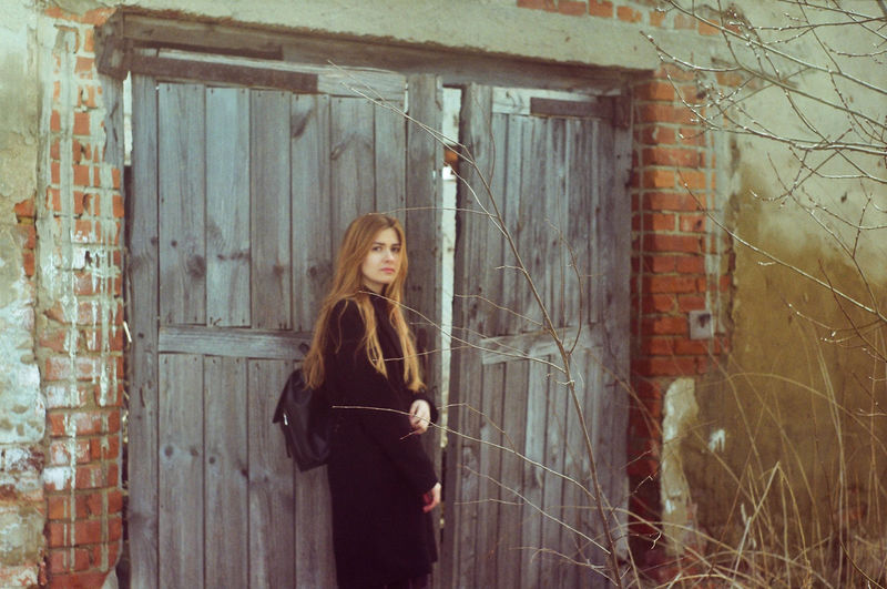 Portrait of woman standing against door of abandoned building
