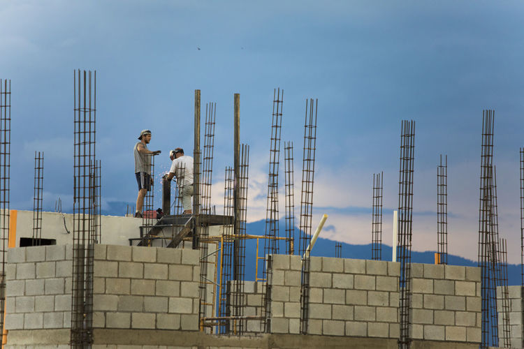 Two construction workers work or rooftop, welding metal railing.