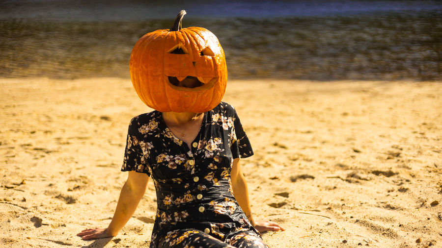 Portrait of woman holding jack o lantern on sand at beach