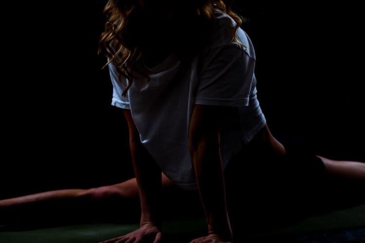 Midsection of woman stretching legs against black background