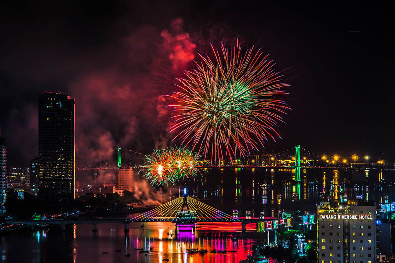 Firework display over illuminated buildings and river in city at night